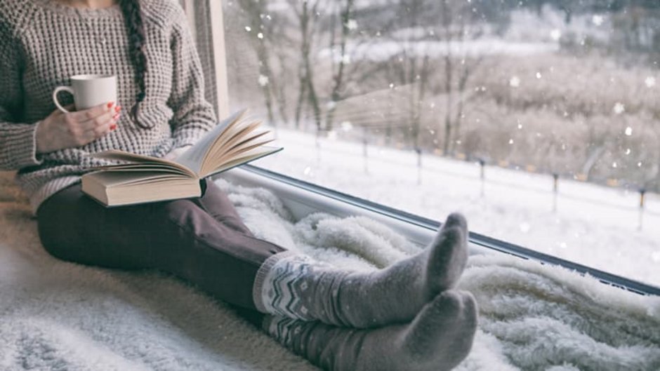 Isolierverglasung, Frau am Fenster mit Tasse und Buch, draußen schneits, Foto: NinaMalyna / stock.adobe.com