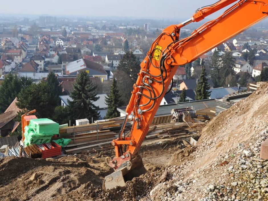 Grundrisse, Baggerarm reicht tief in eine zum Tal hin offene Baugrube hinab. Foto: Hermann / stock.adobe.com