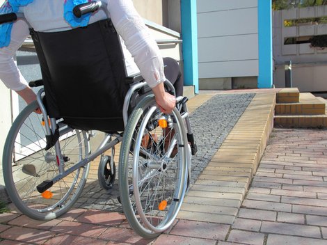 barrierefrei bauen, Person mit Rollstuhl vor Rampe, die zu eine Tür führt, Foto: RioPatuca Images / fotolia.de