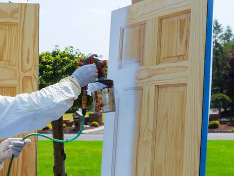 Türen streichen, Handwerker mit weißer Schutzkleidung spritzt Holztür weiß an, Foto: photovs / iStock