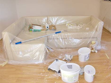 Decke streichen, zu streichendes Zimmer in dessen Mitte ein Soga steht, das mit Folie abgedeckt wurde. Foto: Svenni / stock.adobe.com