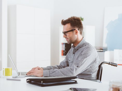 barrierefrei bauen, barrierefreies Arbeitszimmer, Mann im Rollstuhl sitzt am Laptop, Foto: izusek / iStock