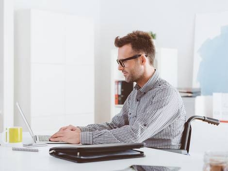 barrierefrei bauen, barrierefreies Arbeitszimmer, Mann im Rollstuhl sitzt am Laptop, Foto: izusek / iStock