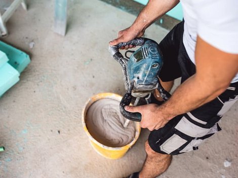 Wand verputzen, Heimwerker rührt Putz in Eimer mit Maschine an. Foto: iStock.com / Pankration
