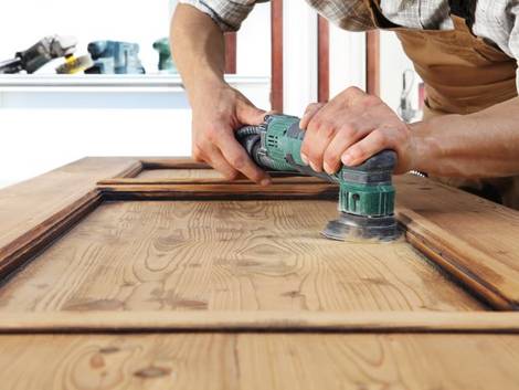 Türen streichen, Holztür, Handwerker schleift liegende Holztür mit Vibrationsschleifer ab, Foto: Visivasnc / iStock