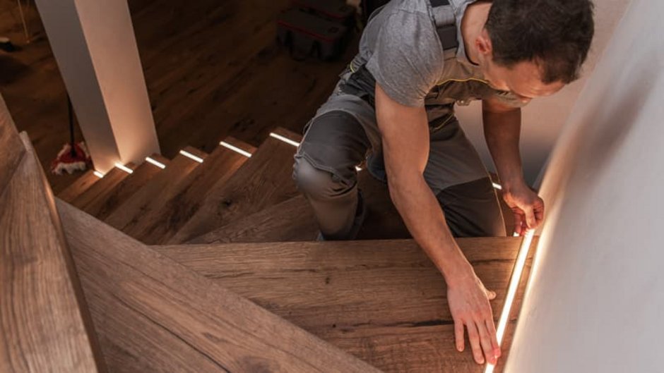 Beleuchtung, Handwerker klebt Leuchtstreifen auf Treppenstufen, Foto: Thomasz Zajda