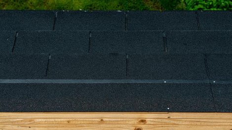 Dachpappe, Gartenhausdach von oben, zu sehen ist der Holzuntergrund, die Dachpappe und ein schmaler Streifen Rasen. Foto: LitterART / stock.adobe.com