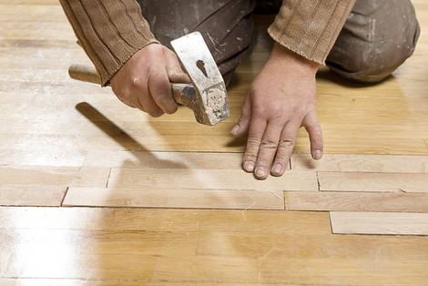 Handwerker kniet am Boden und klopft Holzstücke im Parkett fest, Foto: uwimages/fotolia.com