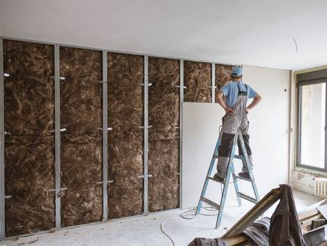 Leichtbauwand, Trockenbauwand, Arbeiter steht auf einer Leiter vor einer halboffenen Leichtbauwand, gefüllt mit braunem Dämmmaterial, Foto: FluxFactory / iStock