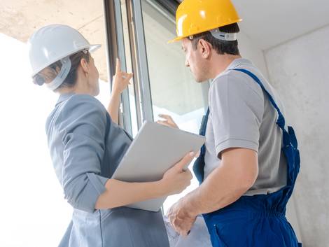 Bauabnahme, Bausachverständige mit Klemmbrett deutet auf Fenster, Handwerker sieht zu, Foto: Kzenon / stock.adobe.com