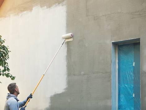 Fassade streichen, Mann streicht mit Teleskoproller eine fensterlose Fassade, Foto: iStock / ronstik