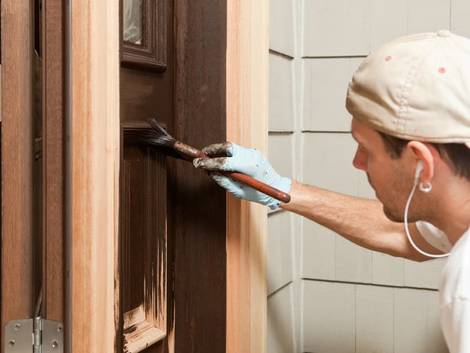 Türen streichen, Handwerker streicht Tür mit Pinsel in brauner Farbe, Foto: BanksPhotos / iStock